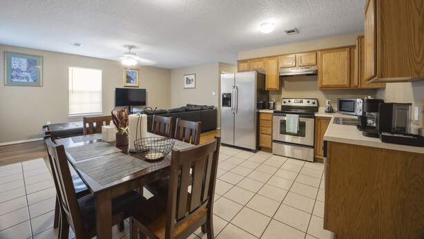 A modern kitchen with wooden cabinets, a dining table with chairs, a refrigerator, stove, microwave, and a television. - Cheerful 2 Bedrooms 2 Full Bathrooms Duplex (Fort Smith)