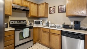 A kitchen with wooden cabinets, stainless steel appliances, a microwave, a coffee maker, and a dishwasher. - Cheerful 2 Bedrooms 2 Full Bathrooms Duplex (Fort Smith)