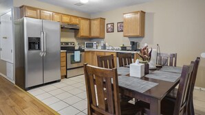 A modern kitchen with wooden cabinets, a stainless steel refrigerator, a microwave, and a dining area with wooden chairs and a table. - Cheerful 2 Bedrooms 2 Full Bathrooms Duplex (Fort Smith)