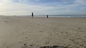 Een breed zandstrand met voetafdrukken en een paar mensen in de verte.