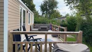 Een houten terras met buitenmeubilair, waaronder een bank en stoelen, en een barbecue.