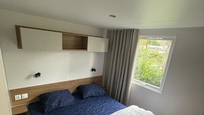 Een slaapkamer met een bed, nachtkastje, raam en een ingebouwde plank boven het bed.