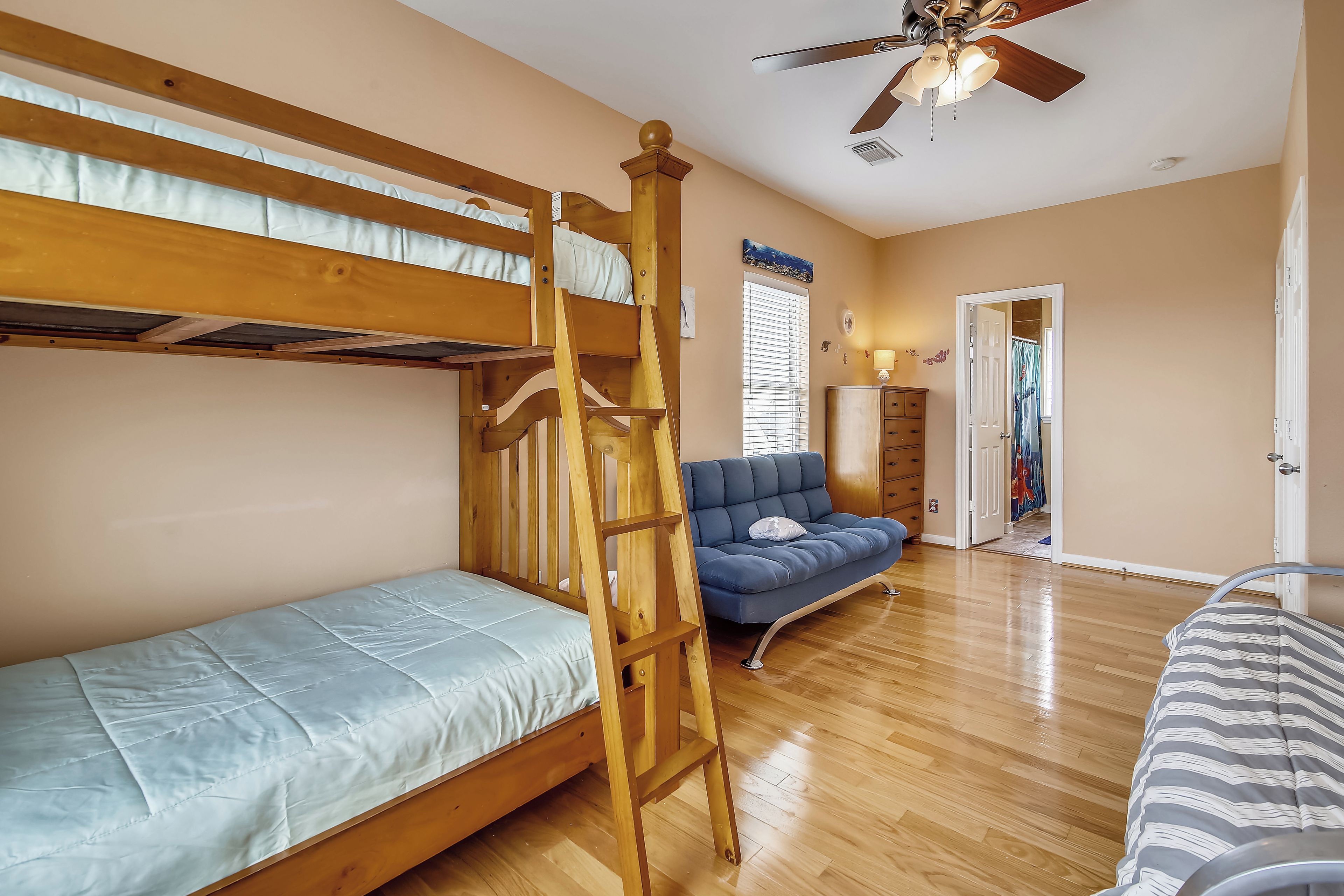 A bunk bed room with a ladder, a sofa, and a ceiling fan.