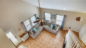 A spacious living room with a large sectional sofa, a ceiling fan, and a view of the outside through windows. - Sunflower Surf by Ryson Vacation Rentals (Galveston)