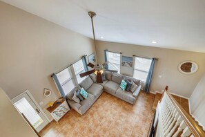 A spacious living room with a large sectional sofa, a ceiling fan, and a view of the outside through windows. - Sunflower Surf by Ryson Vacation Rentals (Galveston)