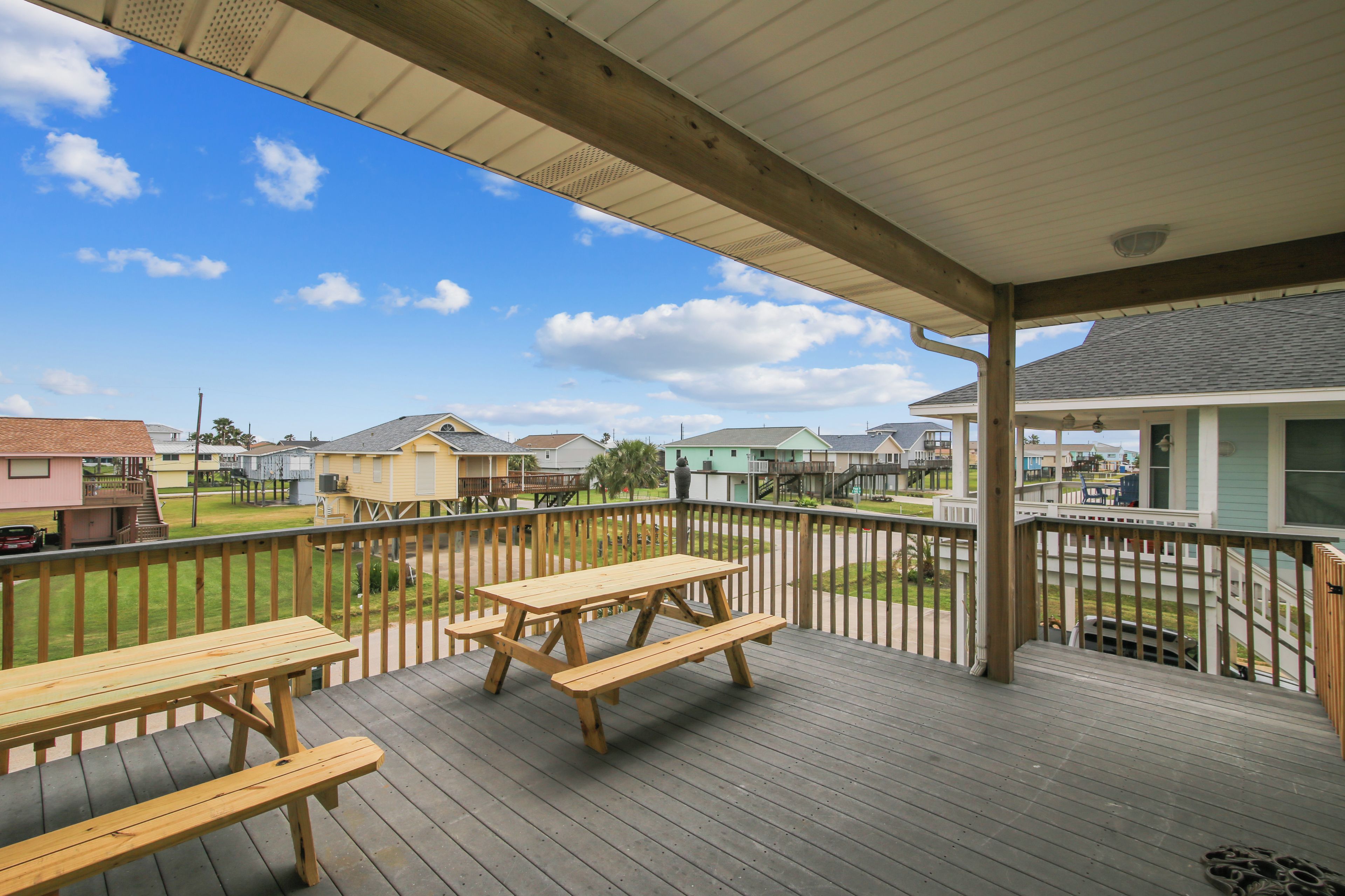 A wooden deck with picnic tables and a view of a residential area.