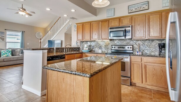 A modern kitchen with wooden cabinets, granite countertops, stainless steel appliances, and a central island. - Sunflower Surf by Ryson Vacation Rentals (Galveston)