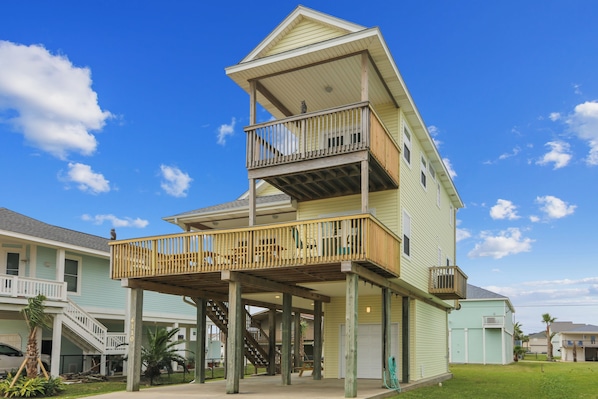 A multi-story building with a balcony on the second floor and a covered area on the first floor. - Sunflower Surf by Ryson Vacation Rentals (Galveston)