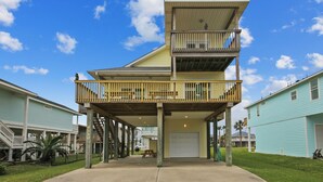 A two-story building with a balcony on the upper floor, a garage, and a staircase leading to the upper level. - Sunflower Surf by Ryson Vacation Rentals (Galveston)