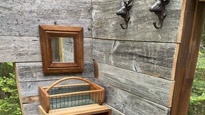 Uma área de estar ao ar livre com bancos de madeira, mesa com churrasqueira de metal e espelho fixado na parede.