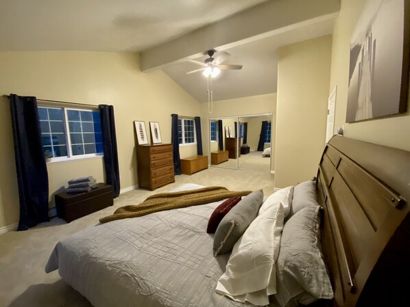 Cozy retreat with a large bed, dresser, and mirror, complete with a ceiling fan and window with curtains.