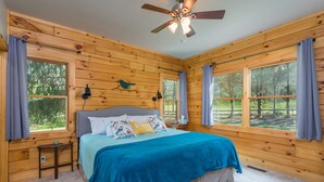 Un dormitorio tipo cabaña de madera con una cama, un ventilador de techo y ventanas amplias.
