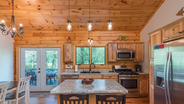 Cocina de cabaña de madera con encimeras de granito, una isla central y un refrigerador de acero inoxidable.