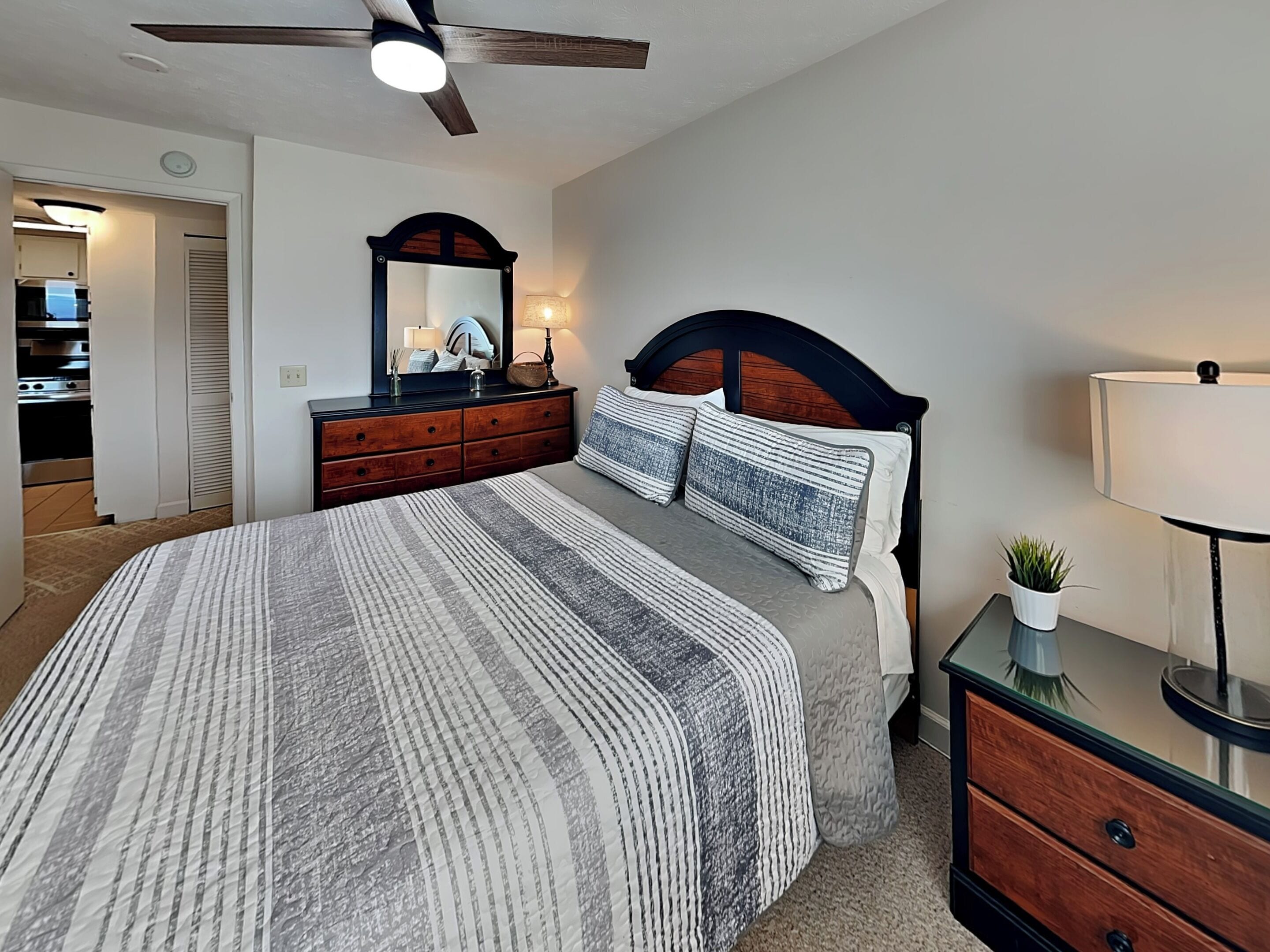 A bedroom with a bed, a dresser, a mirror, a ceiling fan, and a lamp.