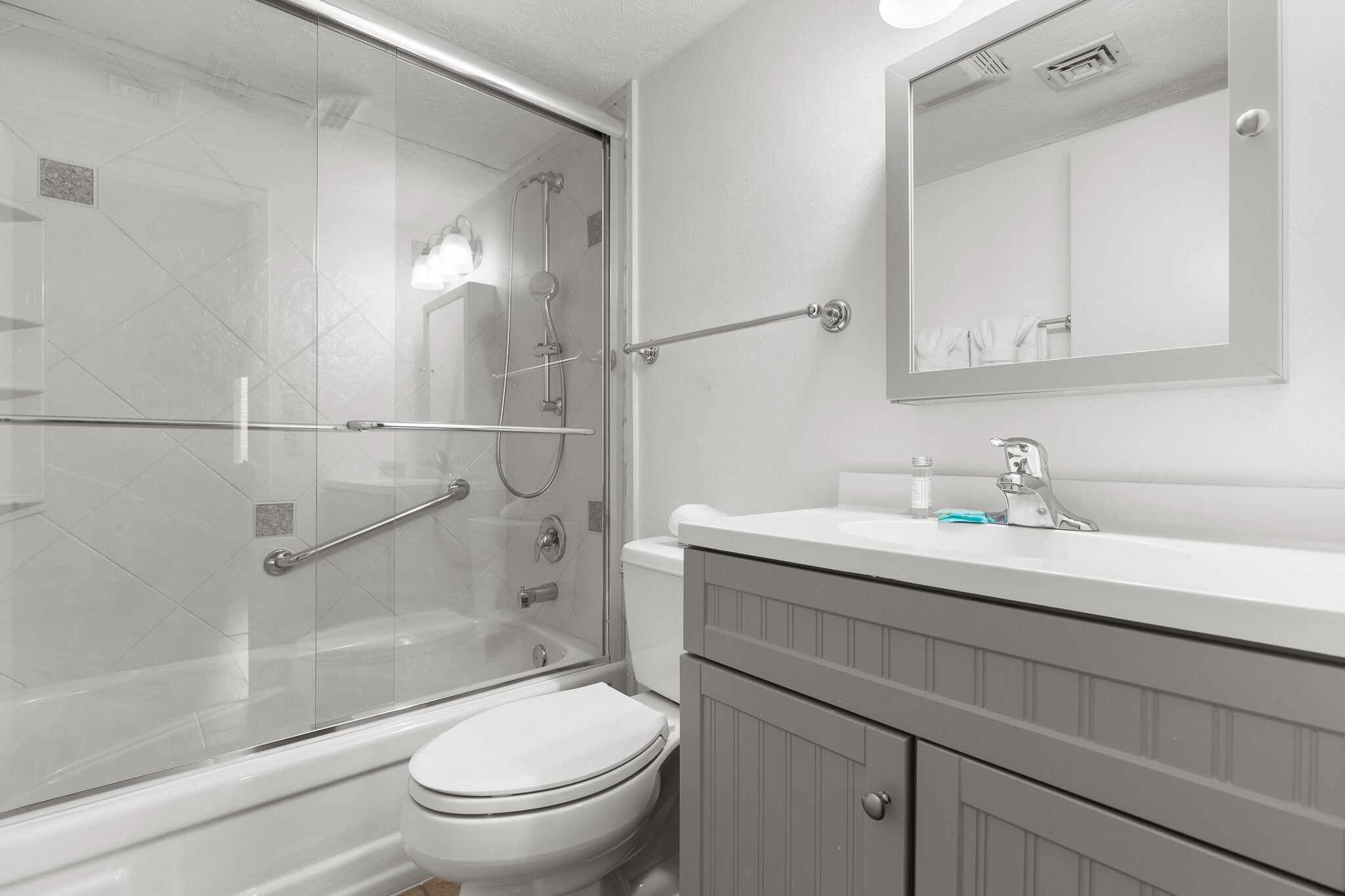 A bathroom with a glass-enclosed shower, a white toilet, and a vanity with a mirror.