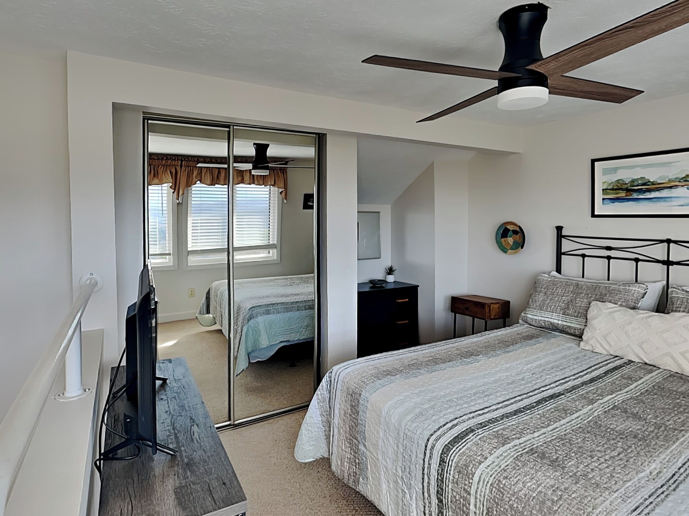 A bedroom with a bed, a ceiling fan, a dresser, a nightstand, and a mirror.