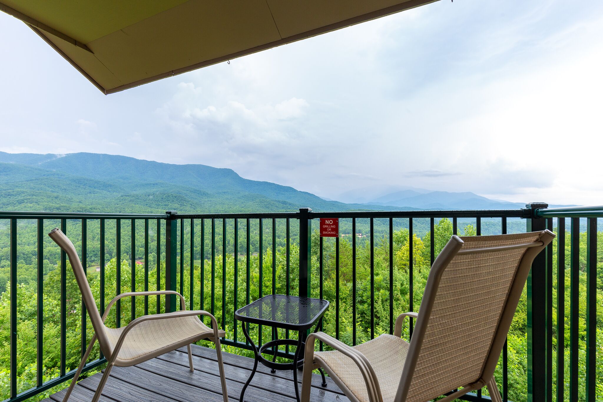 A balcony with two chairs and a small table, overlooking a lush green landscape with mountains in the distance.