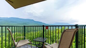 A balcony with two chairs and a small table, overlooking a lush green landscape with mountains in the distance.