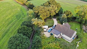 Eine Vogelperspektive eines Hauses, umgeben von üppiger Vegetation, mit einer Auffahrt zu einer Garage und einem geparkten Auto davor.