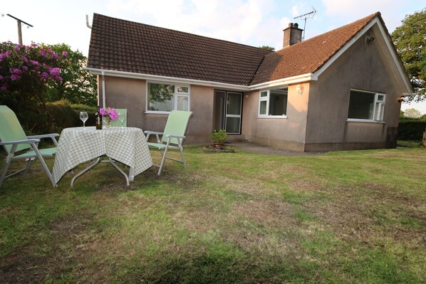 A house with a brown tiled roof, a small front yard, and a table with chairs outside. - Woodlands (Okehampton)