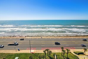 A coastal road with a parking lot, beach, and ocean view. - Pelican View by Ryson Vacation Rentals (Galveston)