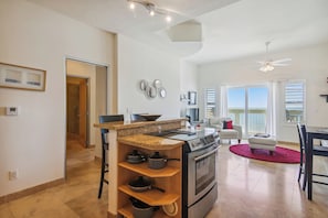 A modern kitchen with a built-in oven and stove, a granite countertop, and a dining area with a red rug and a white chair.