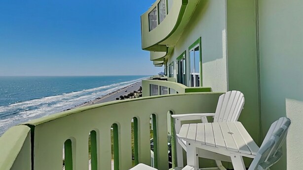 A balcony with white chairs, a view of the ocean, and a building with a green facade. - Pelican View by Ryson Vacation Rentals (Galveston)