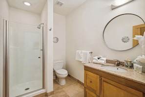 A bathroom with a glass-enclosed shower, a toilet, a sink with a vanity, and a round mirror on the wall. - Pelican View by Ryson Vacation Rentals (Galveston)