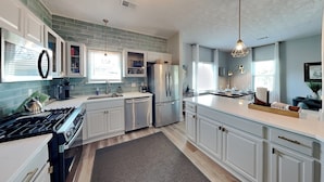 A modern kitchen with white cabinets, a stainless steel refrigerator, and a built-in oven. - The Blue Flamingo by Ryson Vacation Rentals (Galveston)