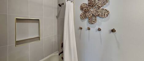 Un baño con bañera, cortina de ducha, toallero y soporte para papel higiénico.