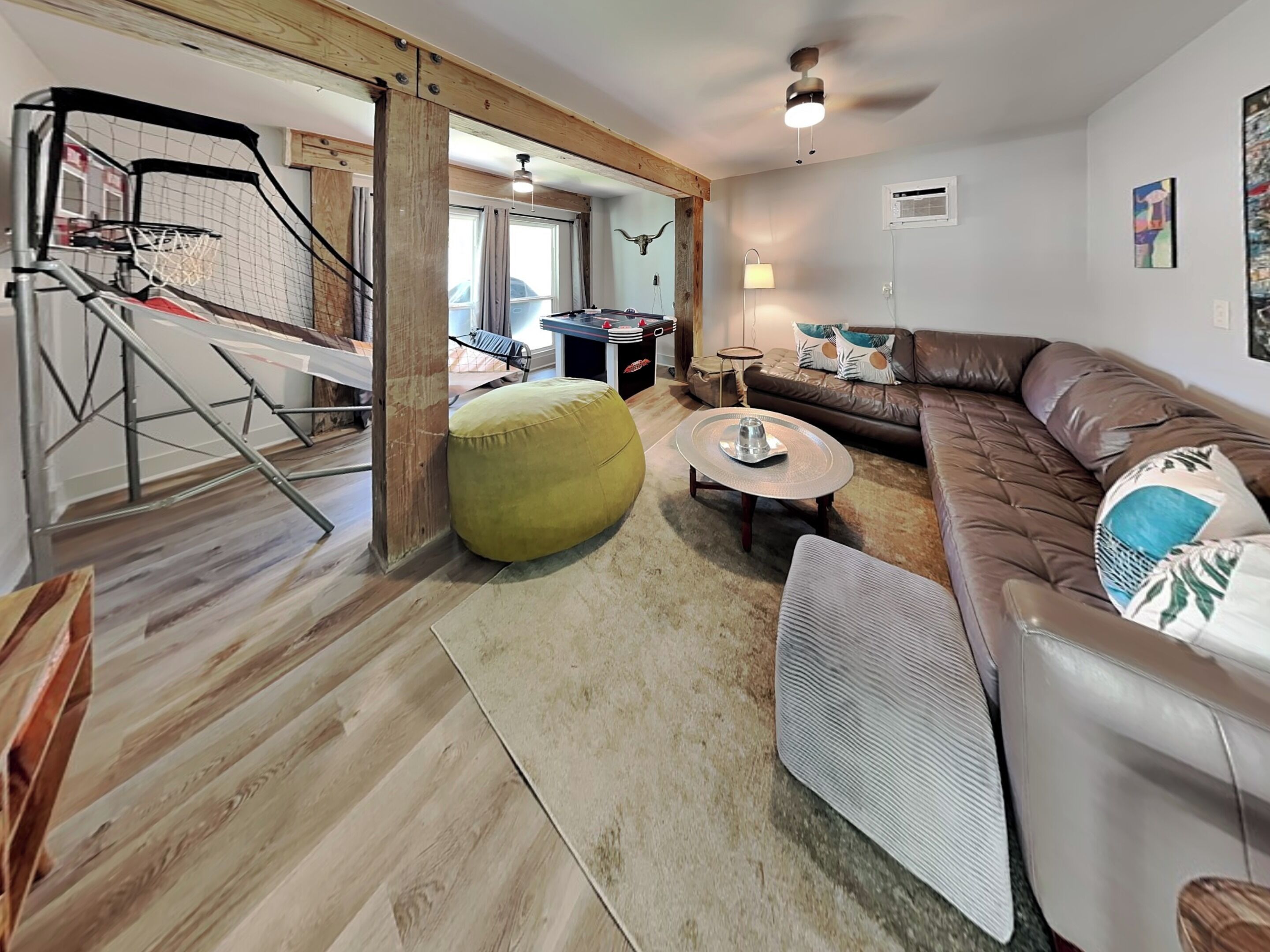 Ein modernes Wohnzimmer mit Basketballkorb, einem grünen Sitzsack, einem runden Couchtisch und einem braunen Ledersofa.
