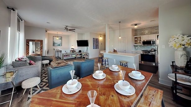 A modern kitchen with a central island, a dining area with a wooden table set for six, and a living area with a sofa and a TV. - The Blue Flamingo by Ryson Vacation Rentals (Galveston)