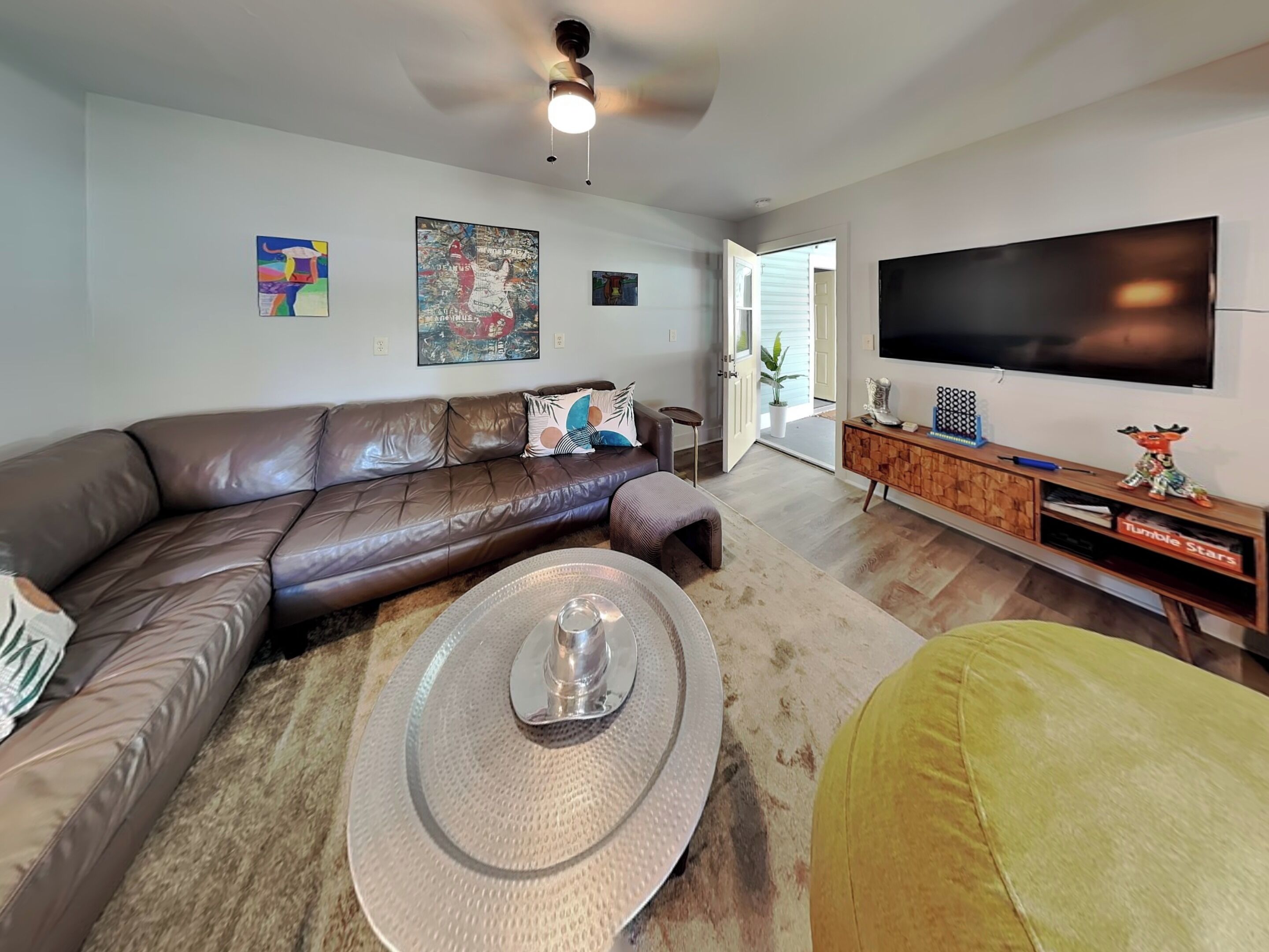 Una sala de estar con un sofá de cuero marrón, una mesa de centro, un televisor y un mueble de madera para entretenimiento.