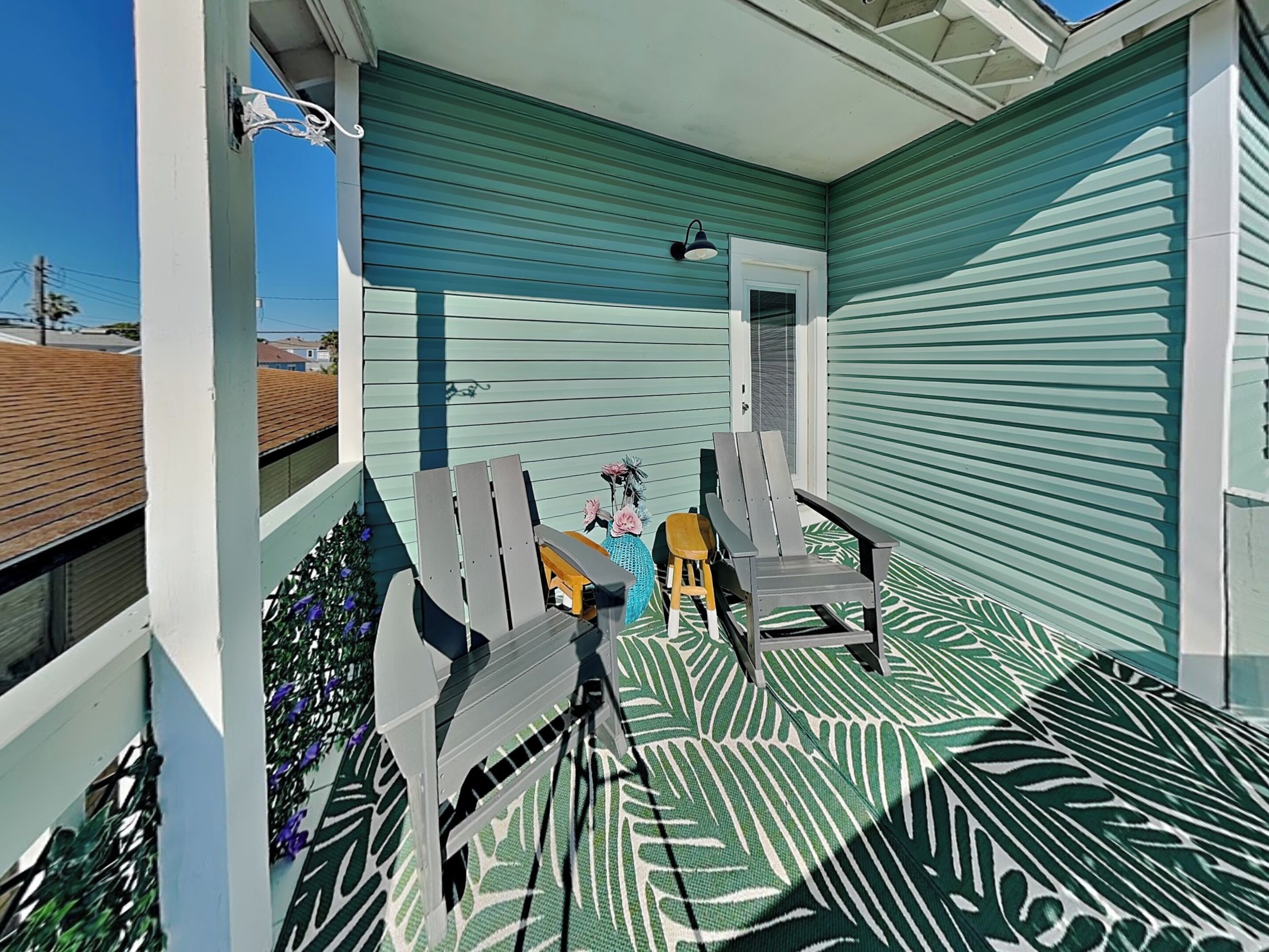A covered porch with two Adirondack chairs, a small table, and a potted plant.