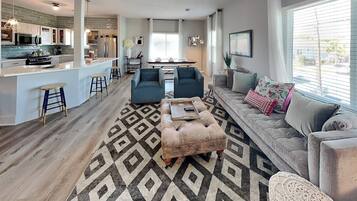 Una sala de estar moderna con sofá, reposapiés y mesa de centro, un área de cocina con barra y un espacio para comer.
