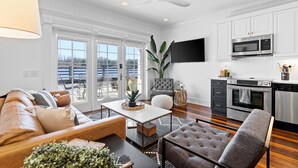 A modern living room with a sofa, coffee table, and armchairs, a kitchen with stainless steel appliances, and a large window with a view. - Waterfront, Sunset Views! Historic Dwtn-King Bed-Luxury with Free Parking!  (Wilmington)