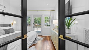 A modern bedroom with a large bed, a dresser, and a view of the outdoors through a glass door. - Waterfront, Sunset Views! Historic Dwtn-King Bed-Luxury with Free Parking!  (Wilmington)