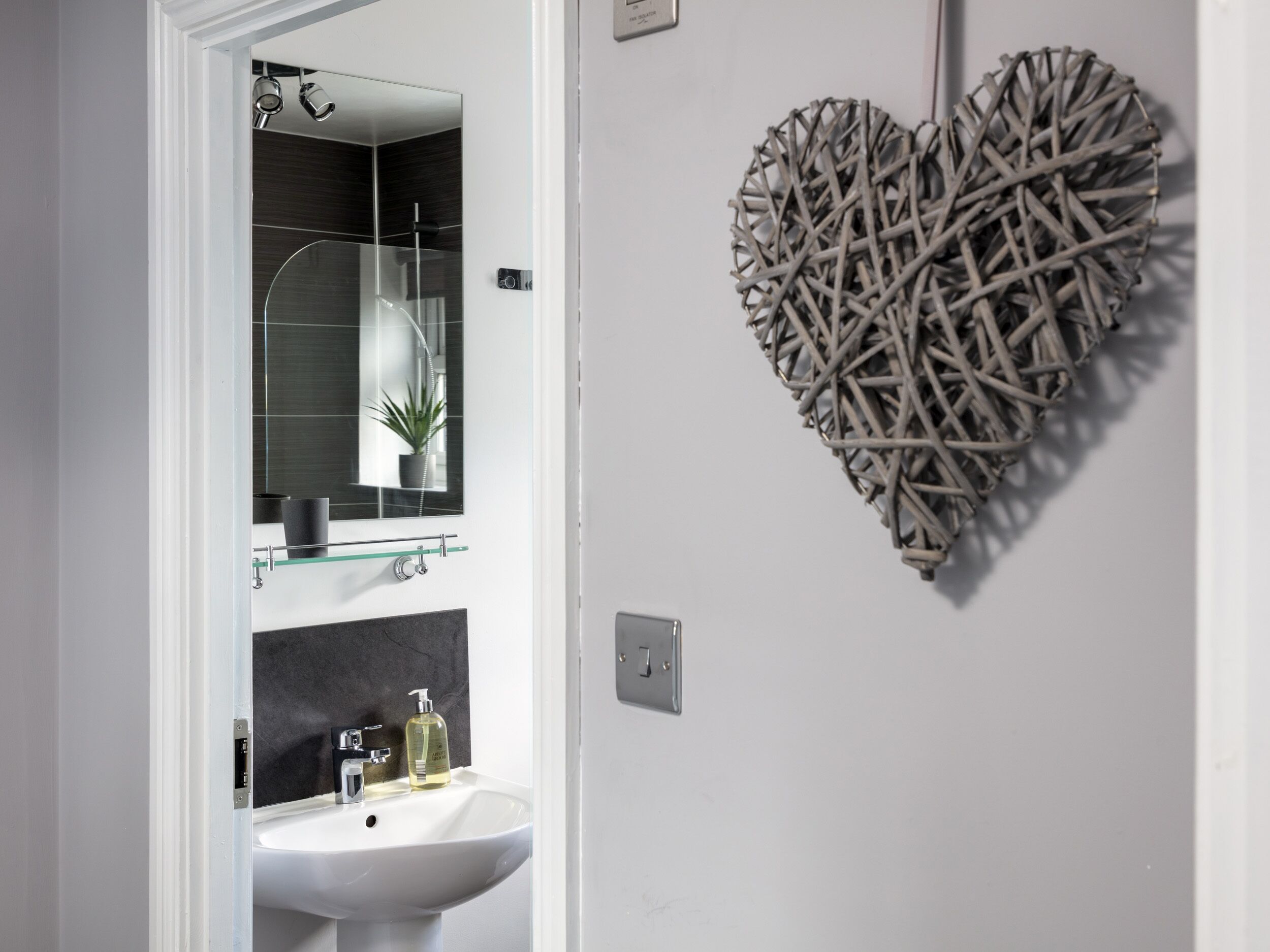 A bathroom with a white sink, a mirror, and a decorative heart-shaped wall piece.