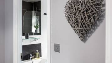 A bathroom with a white sink, a mirror, and a decorative heart-shaped wall piece.