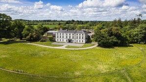 A large, white, multi-story building with a symmetrical facade, surrounded by a well-maintained lawn and trees. - 2 Bed Suite With Tea/coffee Making Facilities (Kells)