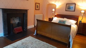 A bedroom with a wooden bed, a fireplace, a radiator, and two bedside lamps. - 2 Bed Suite With Tea/coffee Making Facilities (Kells)