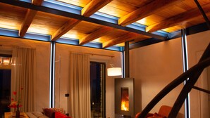 A modern living room with a sofa, a table with books and a vase, a fireplace, and a view through large windows. - Wonderful Private Villa With Pool in Riparbella (Riparbella)