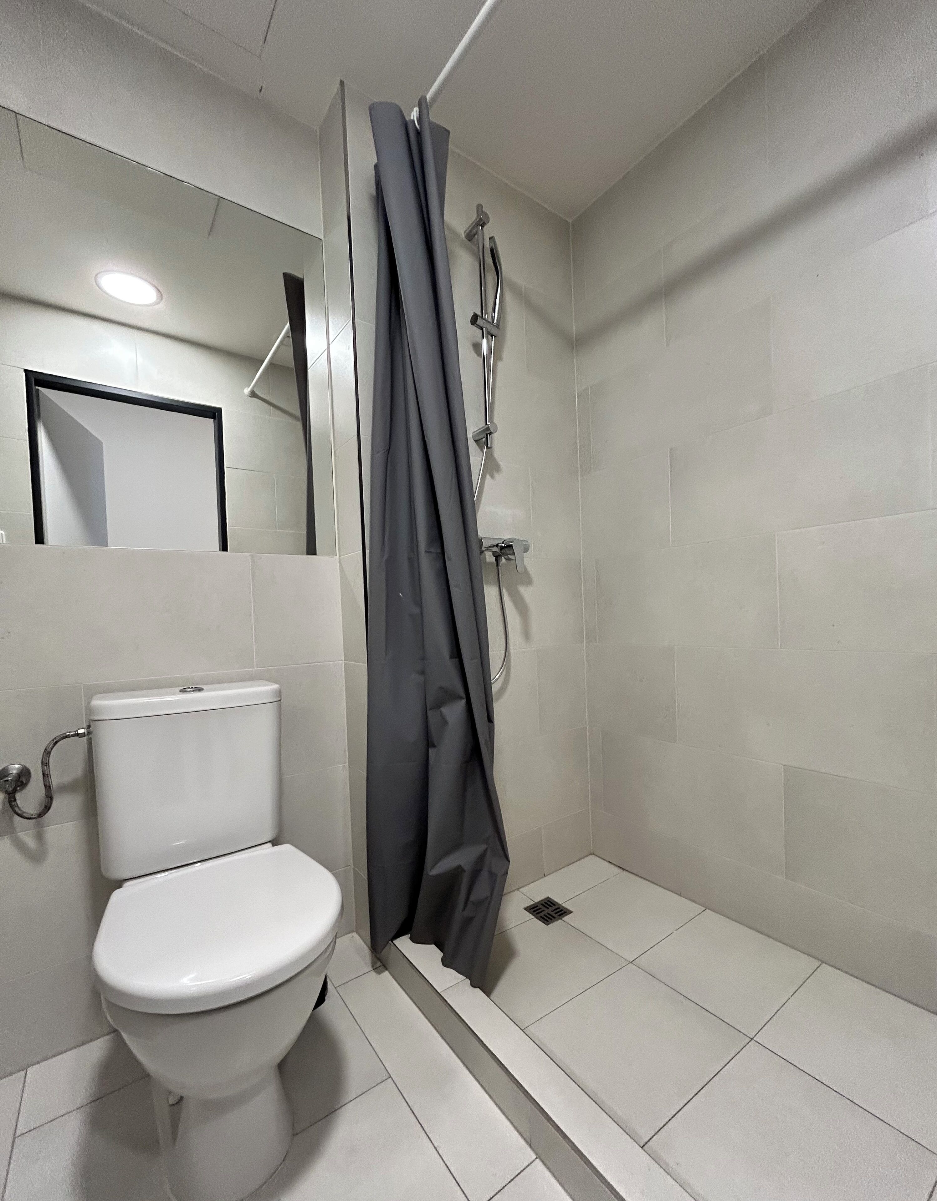 Un bagno con un water, una doccia con tenda e uno specchio a parete.