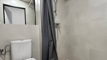 Un bagno con un water, una doccia con tenda e uno specchio a parete.
