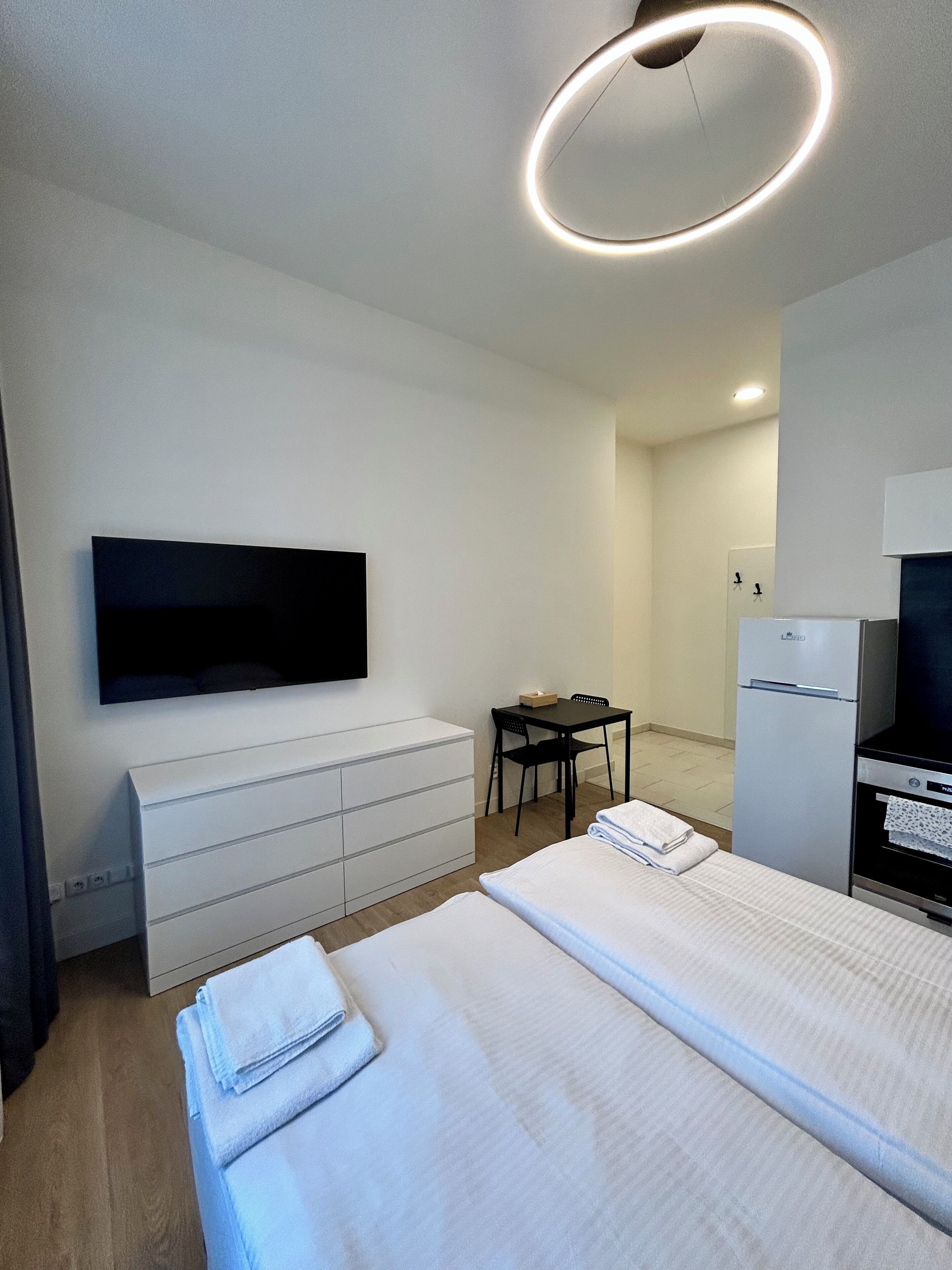 Een moderne hotelkamer met een bed, een bureau, een flatscreen-televisie, een minibar en een plafondlamp.