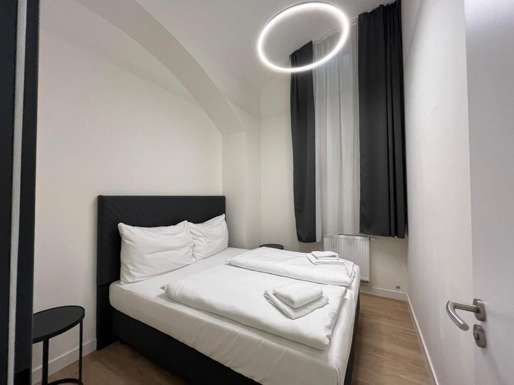 A modern hotel room with a neatly made bed, a small side table, and a large window with curtains.