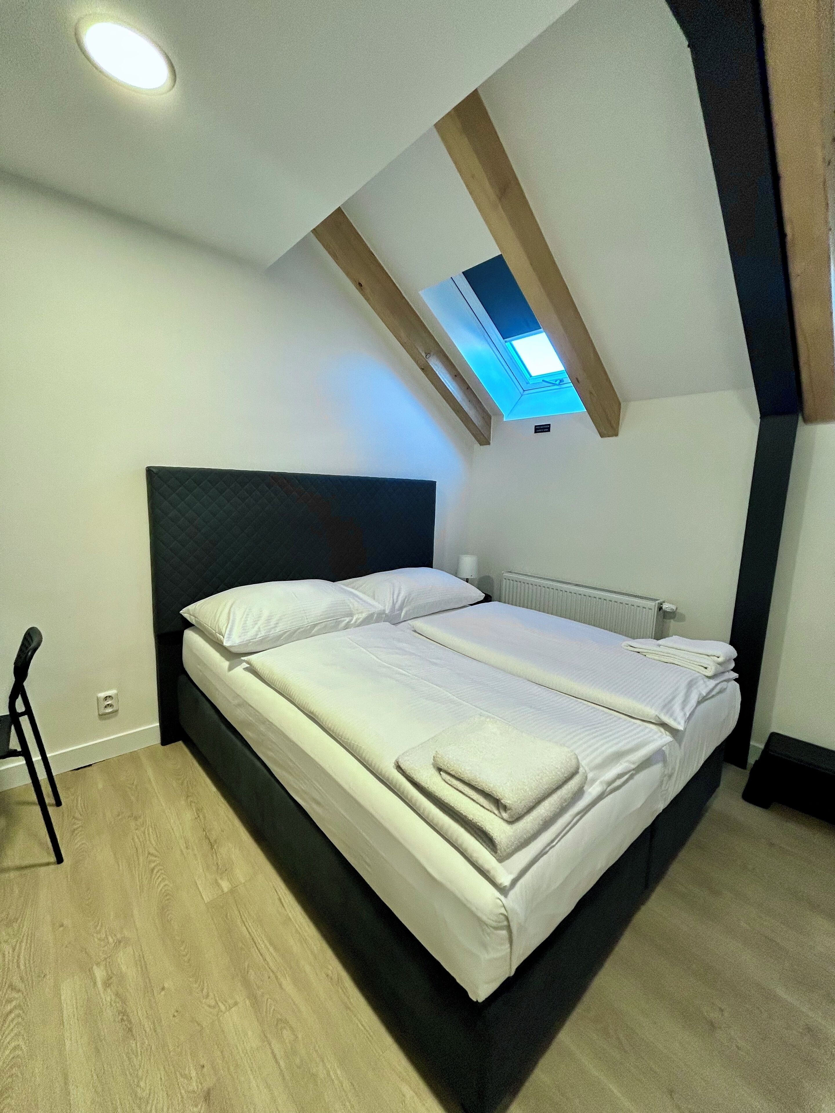 Une chambre à coucher avec un lit, une lucarne, un radiateur et un plancher en bois.