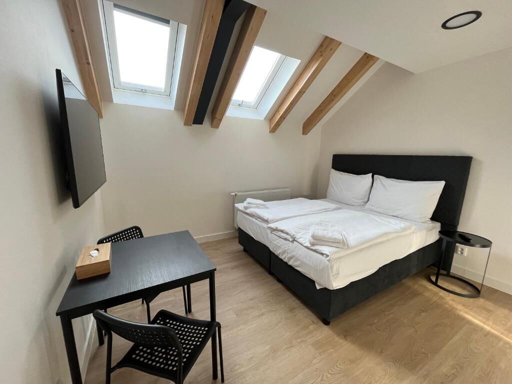 A bedroom with a bed, a desk, two chairs, a TV, and skylights.