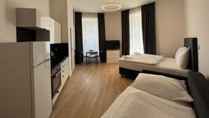 Habitación de hotel compacta con kitchenette, una cama individual, un escritorio y una silla.
