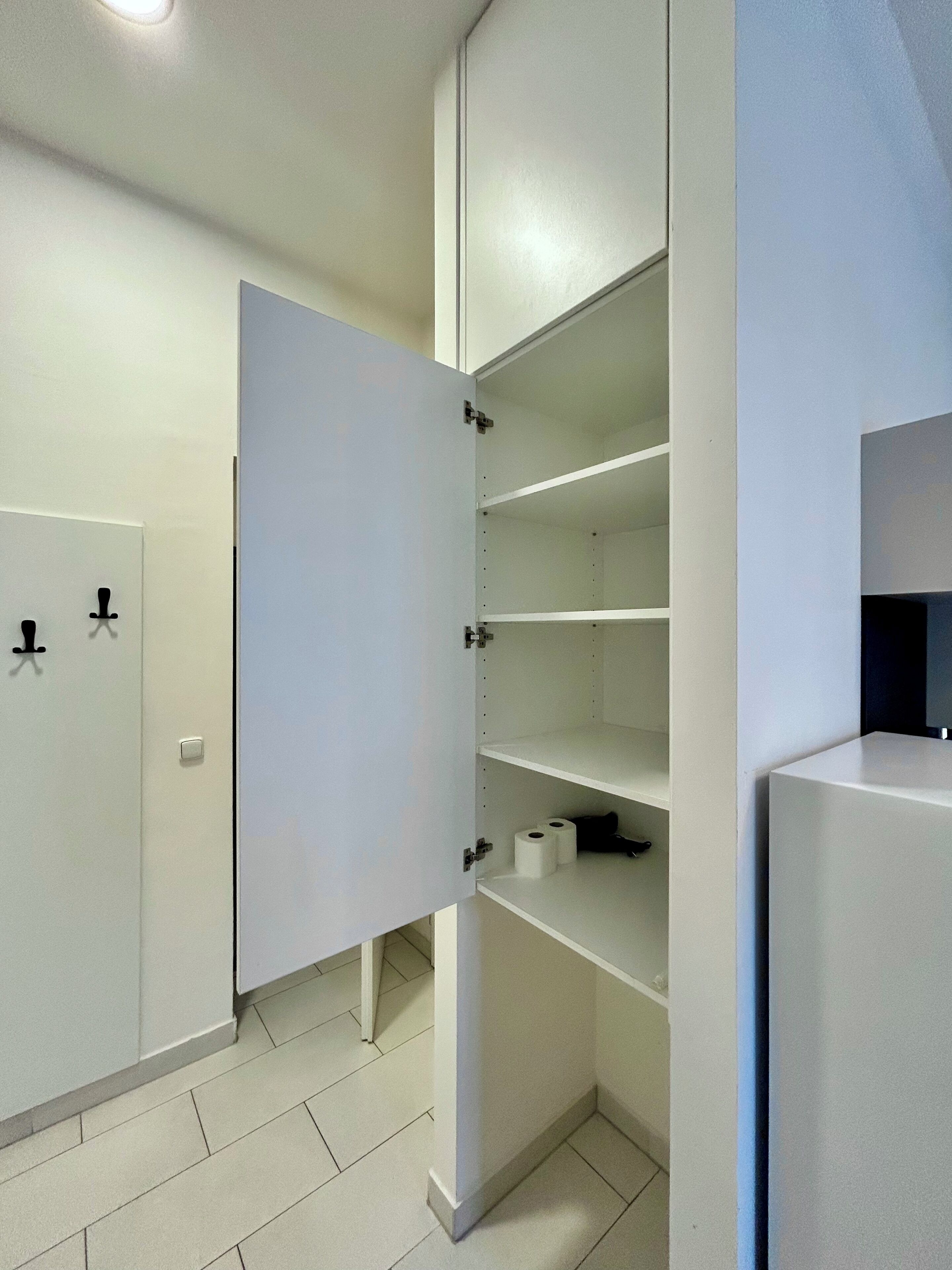 Een inpandige kast met open deuren, waarin planken en een klein vak zichtbaar zijn.